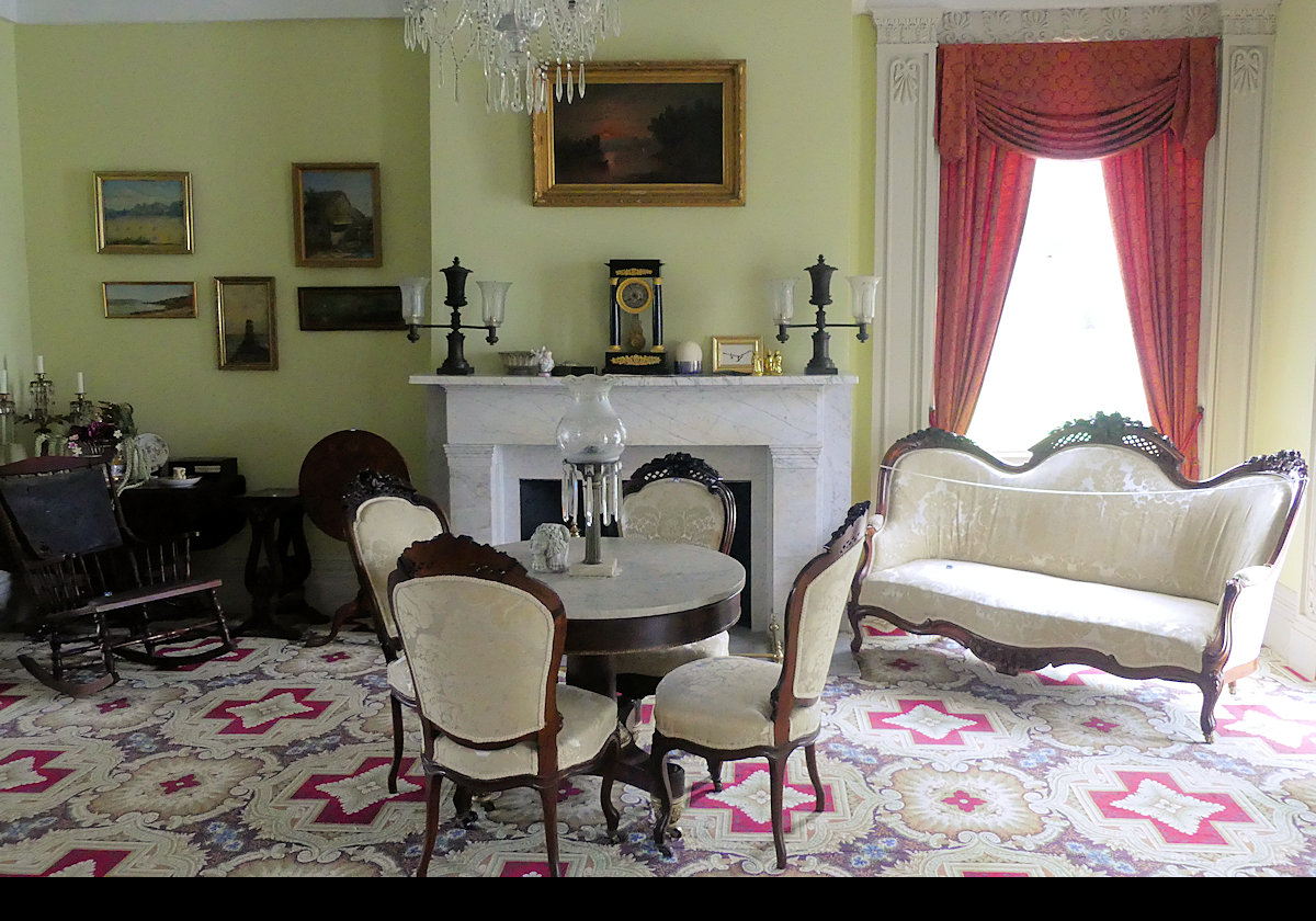 A living room with a card table set up . Note the interesting clock on the mantle. The next picture has a close-up of the clock.