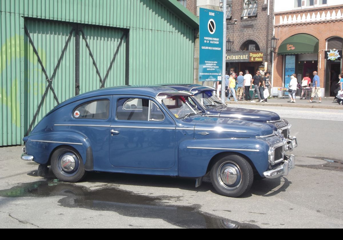 A pair of vintage Volvos.  The near one seems to be a Volvo 444, probably from the 1950s with the split windscreen  Behind it is a 544 sporting the single curved windscreen.