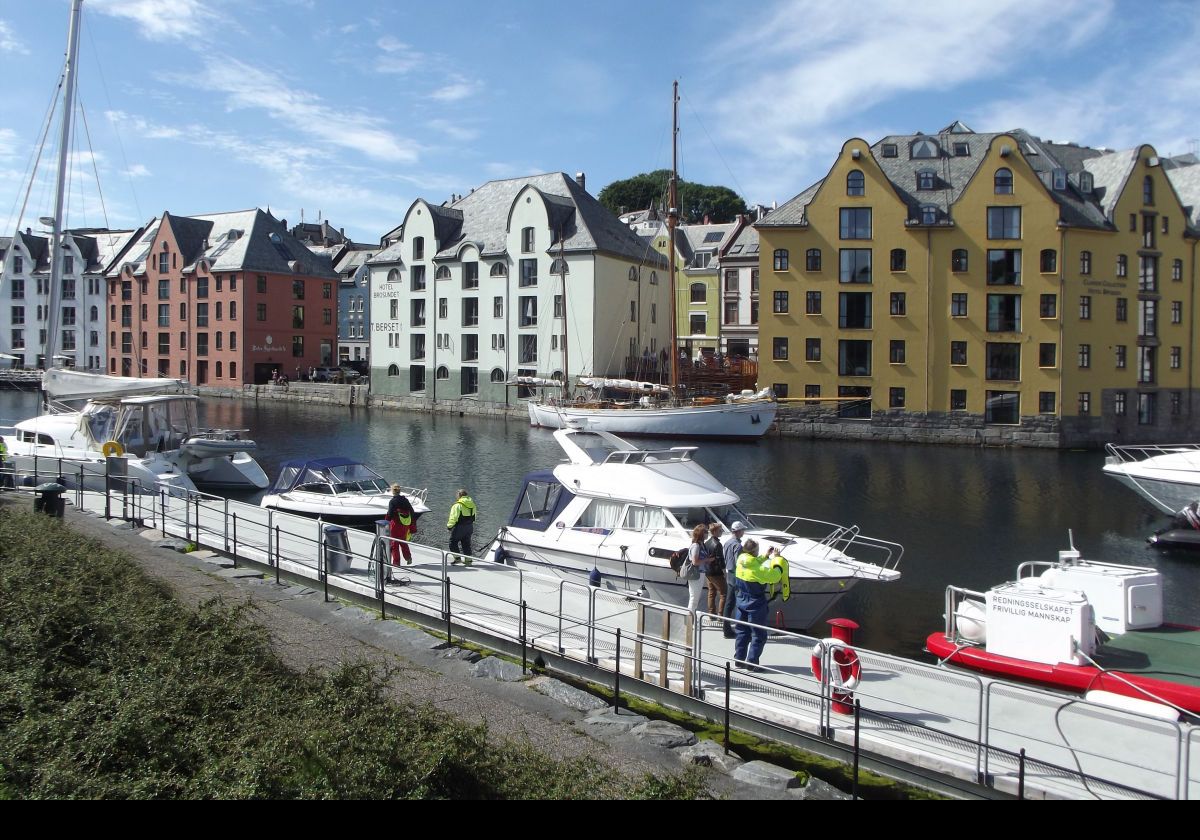 The brown building to the left is Peter Spjelkavik A/S Shipping & Marine Supplier, the white building is the Hotel Brosundet, and the ochre building is the Hotel Bryggen. The waterway separates the islands of Aspøy and Nørvøya; two of the 7 islands that comprise Alesund.